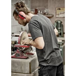 A man wearing a grey T-shirt works on a machine in a workshop, with safety glasses and earmuffs.