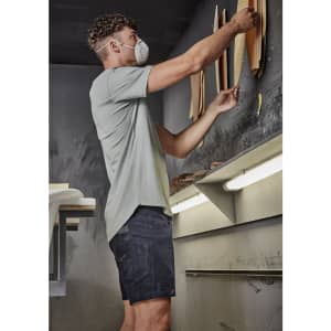 A man wearing a light grey t-shirt and dark shorts adjusts materials on a wall in a workshop setting.