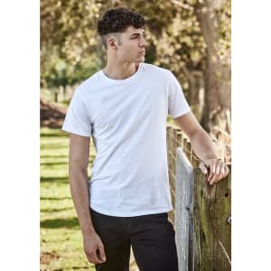A white men's T-shirt is worn by a model standing beside a wooden fence in an outdoor setting.