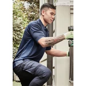 A man wearing a navy blue short sleeve polo with a patterned side panel is kneeling near equipment outdoors.