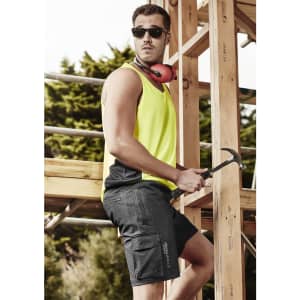 A man in a bright yellow and black Hi Vis singlet, wearing sunglasses and holding a hammer, stands near scaffolding.