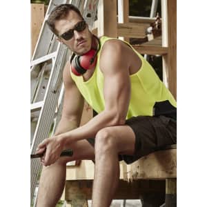 A man in a high visibility yellow singlet and dark shorts, wearing sunglasses and ear protection, seated at a construction site.