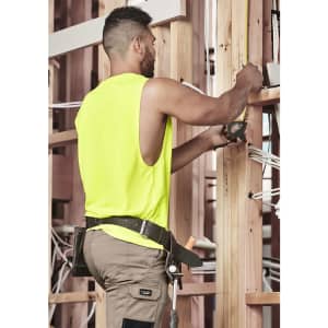 A man wearing a high visibility sleeveless tee in fluorescent yellow, working on wooden framing with tools.