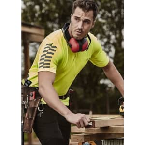 A man wears a high-visibility yellow short sleeve polo shirt with black stripes, featuring a logo. He is outdoors, working.