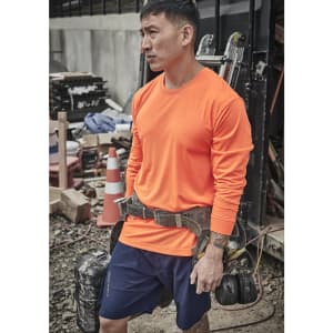 A man wearing an orange long sleeve high visibility tee is standing at a construction site, equipped with a tool belt.