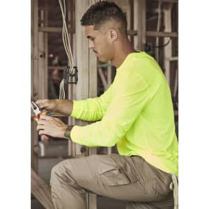 A man works in a construction setting, wearing a neon yellow long sleeve tee and beige cargo pants, using pliers.