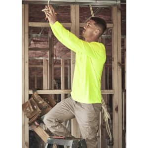 A man in a high visibility long sleeve yellow tee works on a ladder in a construction setting. The shirt has a logo.