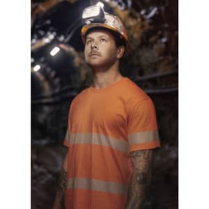 A man wearing an orange hi-vis segmented tape cotton tee shirt and a safety helmet with headlamp, standing in a dimly lit area.