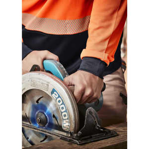 A close-up of hands gripping a circular saw, wearing an orange and navy long sleeve work polo shirt.