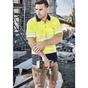 A unisex hi-vis segmented tape short sleeve polo in bright yellow and navy, featuring reflective stripes, held by a man on a worksite.
