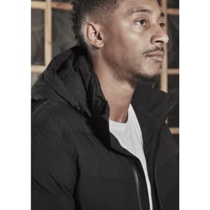 A black hooded puffer jacket, featuring a zipper and a discreet logo, worn by a model.