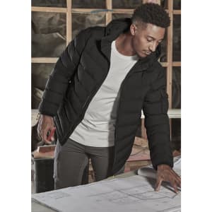 A black unisex puffer jacket with a hood, worn by a person examining blueprints indoors. The jacket has a logo.
