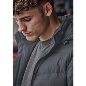 A close-up of a man wearing a dark grey hooded puffer jacket, featuring a zippered front and a casual look.