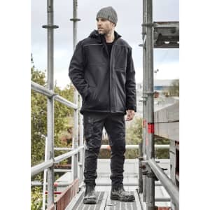 A black unisex softshell jacket worn by a man on scaffolding, with a beanie and work pants, set outdoors.