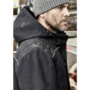 A black unisex softshell jacket with a hood, worn by a man with a grey beanie, features a logo and some dirt stains.