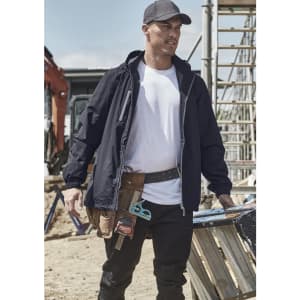 A man wearing a black unisex lightweight packable rain jacket, standing at a construction site with tools and equipment around.