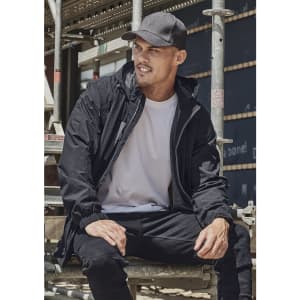 A man wearing a black unisex packable rain jacket sits on scaffolding. The jacket features a hood and has a logo.