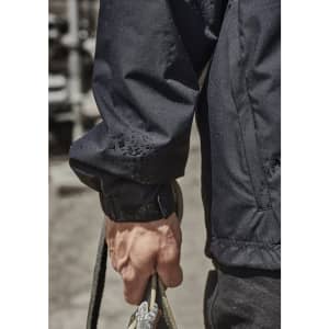 A close-up of a person's arm wearing a black packable rain jacket, holding a rope. The jacket features an adjustable cuff.