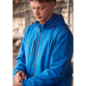 A man in a bright blue unisex rain jacket with a hood, standing indoors near construction. The jacket features a logo.