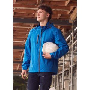 A man wears a blue unisex packable rain jacket, holding a white helmet, set against a construction backdrop.