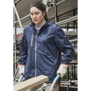 A woman in a navy blue packable rain jacket, wearing gloves, stands near scaffolding, holding a wooden beam.