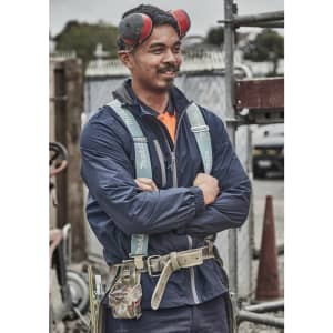 A man in a navy blue packable rain jacket stands with arms crossed, wearing earmuffs and a safety harness.