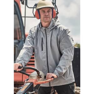 A man wearing a light grey unisex packable rain jacket, with a helmet and ear protection, operating machinery outdoors.