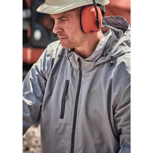 A man wearing a grey unisex packable rain jacket, with ear protection, outdoors in a work environment.