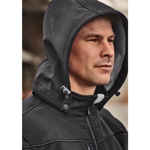 A man wearing a black unisex softshell jacket with a hood, featuring a branded logo on the chest.