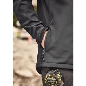 A unisex black softshell jacket featuring a zippered pocket, worn by a person near a measuring tape.