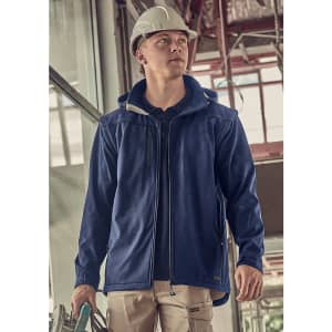 A blue unisex softshell jacket features a hood, shown being worn by a person in a construction setting.