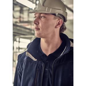 A person wearing a hard hat and a navy blue softshell jacket, looking thoughtfully into the distance.