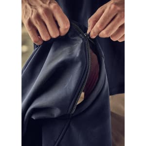 A close-up of hands zipping a navy softshell jacket with a contrasting inner layer. The jacket features a logo.