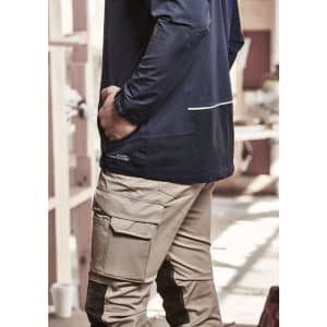 A navy unisex waterproof jacket is worn by a person with their hand in their pocket, paired with beige cargo pants.