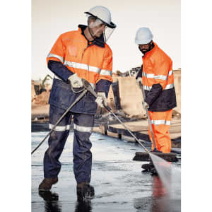 Two men wearing high-visibility orange and navy workwear, including helmets, clean a surface with pressure washers.