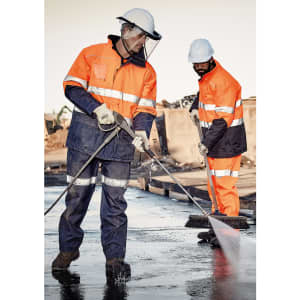 Men wearing high-visibility orange and navy work pants, with safety gear, cleaning a surface at a work site.