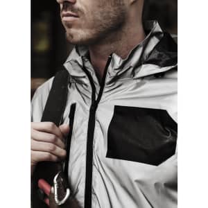 A reflective silver waterproof jacket with a black pocket, featuring a high collar and zip closure, worn by a model.