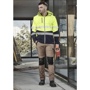 A man wearing a unisex two-tone softshell jacket in high visibility yellow and navy, paired with beige work trousers.