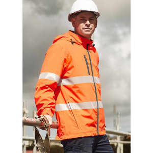 A bright orange packable rain jacket with reflective stripes, worn by a model on a construction site.