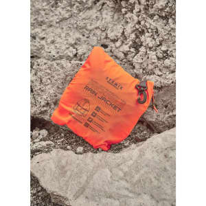 An orange packable rain jacket neatly folded and resting on rocky terrain, featuring a logo and product details.