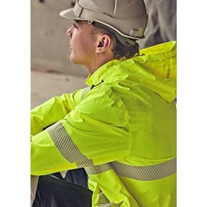 A man in a grey helmet wears a bright yellow rain jacket with reflective stripes, seated in a construction environment.