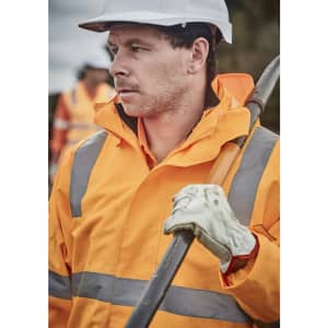 A man wearing an orange waterproof jacket with reflective strips, gloves, and a safety helmet, holding a tool.