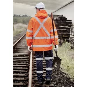 An orange waterproof jacket with reflective stripes, worn by a person holding a shovel, walking along railway tracks.