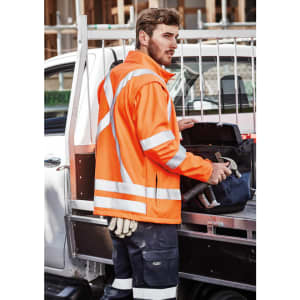 A unisex hi-vis orange softshell jacket with reflective strips, worn by a person holding tools.