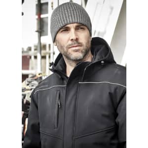 A grey beanie worn by a man in a black jacket, with an industrial background. The beanie features a logo.
