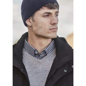 A man wearing a navy beanie, grey sweater, and a checked shirt. The background features a blurred outdoor setting.