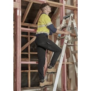 Men's lightweight outdoor cargo pants in black worn by a person on a ladder, set in a construction environment.