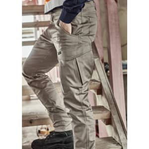 A model wearing beige cargo pants, featuring multiple pockets, standing on a wooden staircase.