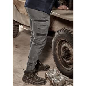 A pair of cuffed heritage work pants in grey, shown with a person standing beside machinery. The pants feature cargo pockets and a logo.