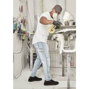 A man wearing light blue stretch jeans and a white t-shirt is spray painting in a workshop.